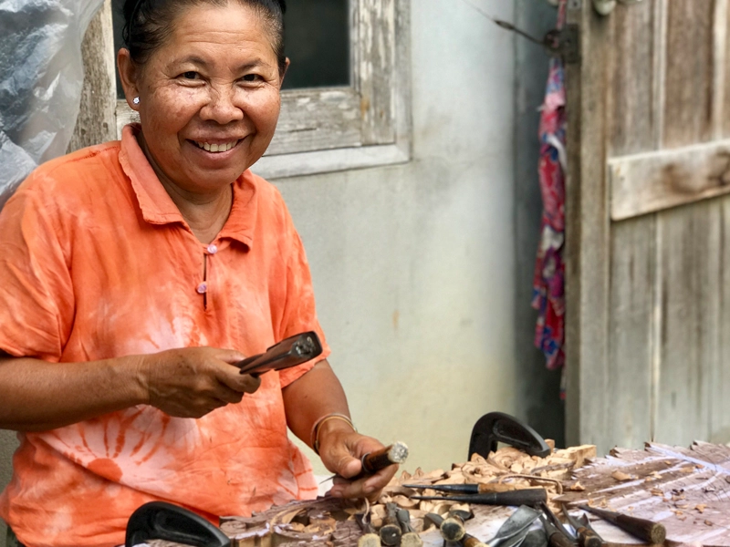 Thai artisan carving a reclaimed wood panel with her hands