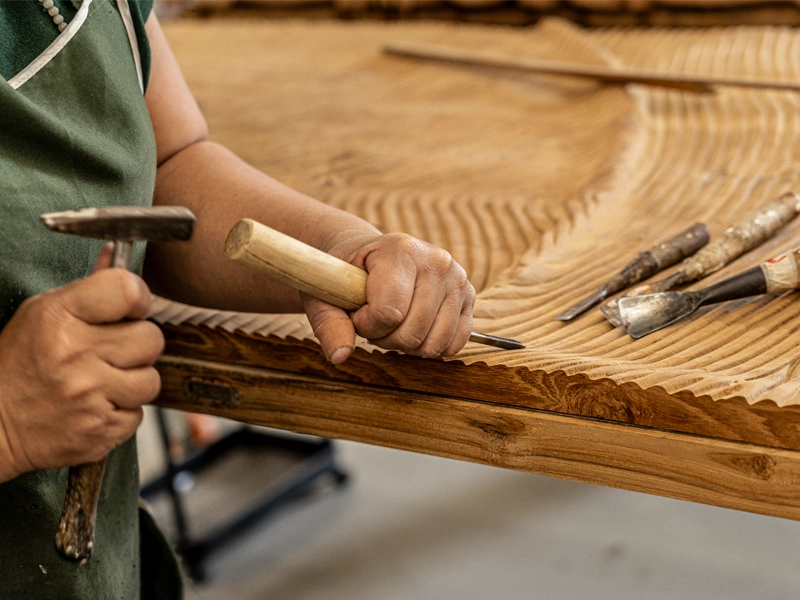 Thai artisan carving wooden headboard by hand with chisel and hammer