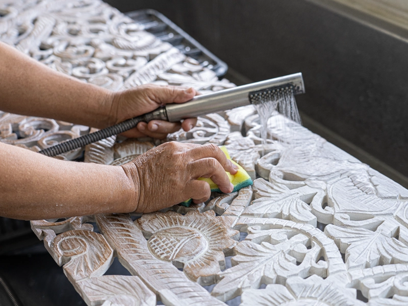 Artisan washing carved teak panel to create a whitewash finish