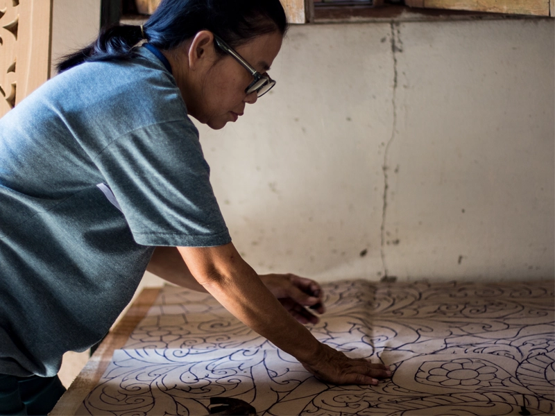 Artisan sketching carved bed headboard design on paper template for wood transfer