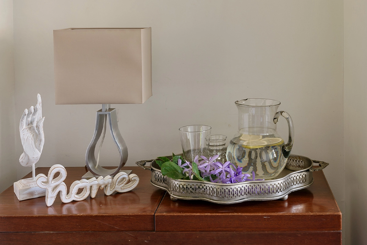 Decorative corner with white wooden ornaments, lamp, and flowers creating a calm Thai-inspired home ambiance.