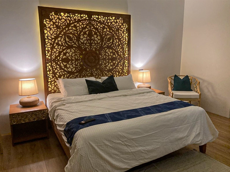 Hand-carved reclaimed teak bed headboard with brown stain and LED backlighting in modern bedroom