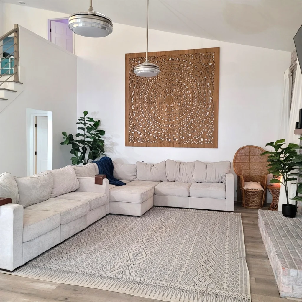 Hand-carved teak wood wall art panel hanging above sofa in modern living room.